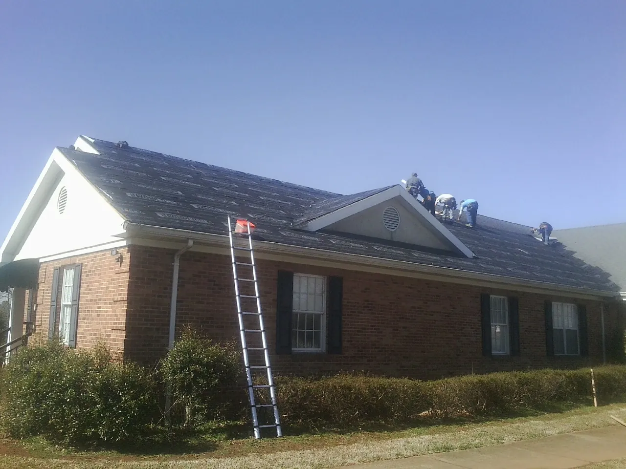 Crew tearing shingles off a brick ranch roof with a ladder set — Emergency Roof Repair work by our crew in Beersheba Springs