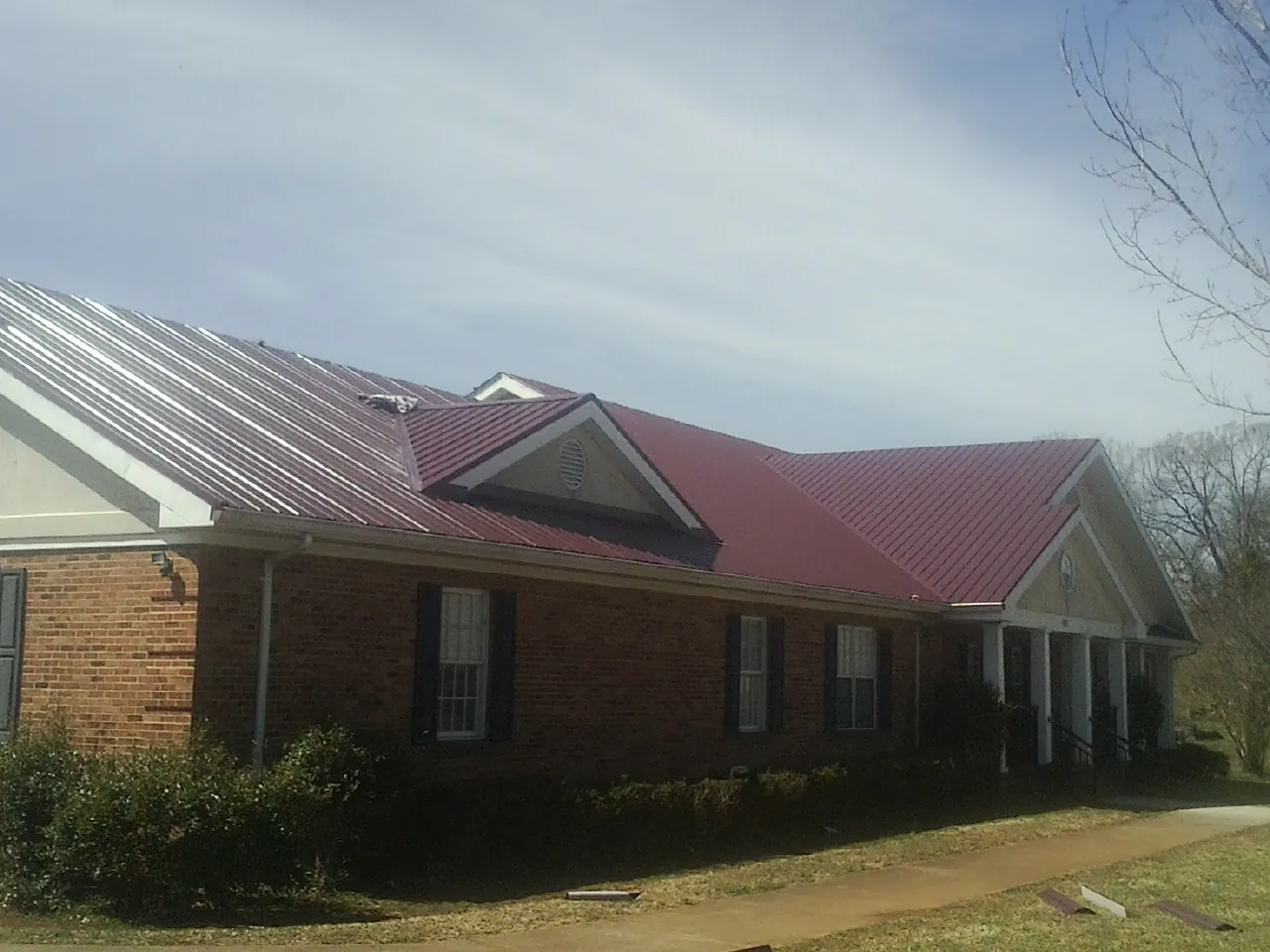Red metal roof with gabled entries on a long brick building, from a Hail Damage Roof Repair job in Beersheba Springs