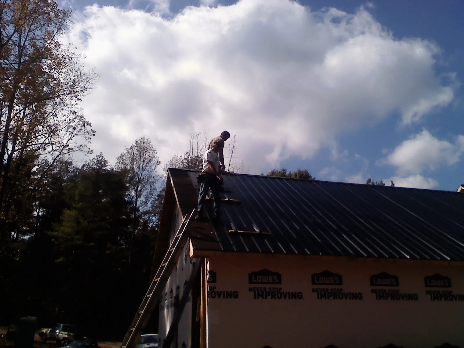 Roofer fastening dark metal panels high against a cloudy sky, from a Roof Inspection job in Beersheba Springs