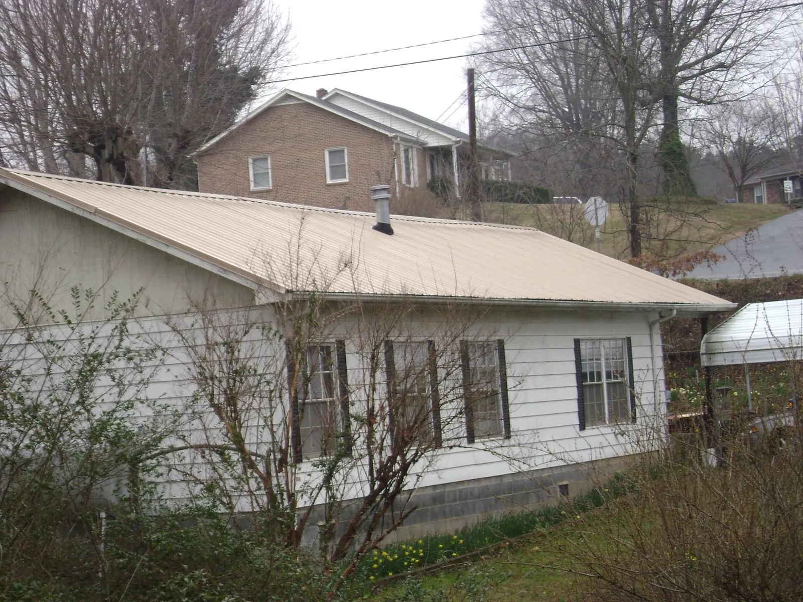 Tan metal roof on a white sided house set into a hillside — Commercial Roofing by Roofing Brothers in Beersheba Springs