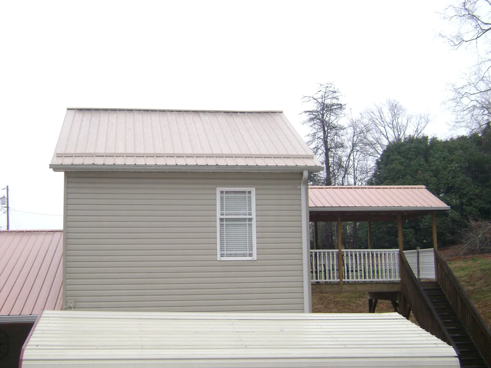 Tan metal roofs on a two story addition and attached porch, from a Roof Replacement job in Beersheba Springs
